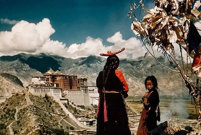 Mother and child pray on Chagpori’s crest, a pilgrim shrine, as incense smolders beneath prayer flags